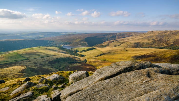 Sunny view with blue sky, from a rocky peak out over open moor and fields, with water in the distance